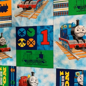 May include: Fabric featuring a repeating pattern of cartoon train characters, including Thomas the Tank Engine and James. The design incorporates blue, red, and green blocks with train tracks, numbers, and the words "BLUE ENGINE".