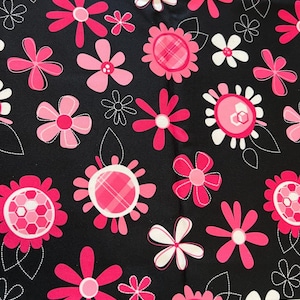May include: Black fabric with a repeating pattern of pink and white flowers. The flowers vary in style, some with plaid centers, others with solid pink petals. White dotted lines and leaves accent the floral design.