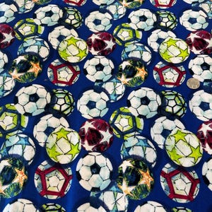 May include: A blue fabric covered with soccer balls in various colors, including white, green, red, and blue. The soccer balls have black pentagon and hexagon patterns. The fabric is suitable for sports-themed projects.
