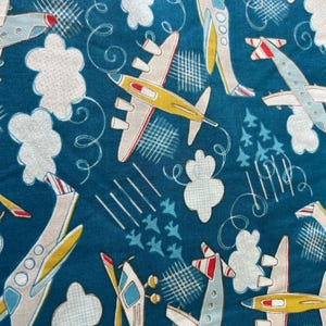 May include: A fabric with a repeating pattern of vintage airplanes, clouds, and stylized contrails on a teal background. The planes are primarily white, yellow, and red, with propeller and jet engine designs. White fluffy clouds and curved lines add to the whimsical design.