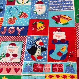 May include: A festive cotton fabric featuring a patchwork design of Christmas-themed illustrations including snowmen, penguins, Santa Claus, bells, Christmas trees, and wrapped gifts. The pattern includes the text Happy Holidays and JOY.