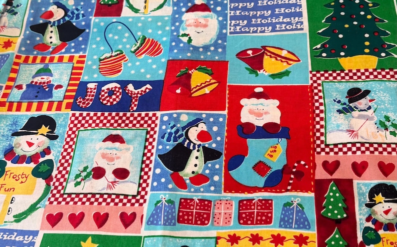K&ouml;nnte beinhalten: Ein festlicher Baumwollstoff mit einem Patchwork-Design aus weihnachtlichen Illustrationen, darunter Schneem&auml;nner, Pinguine, Weihnachtsm&auml;nner, Glocken, Tannenb&auml;ume und verpackte Geschenke. Das Muster enth&auml;lt den Text Happy Holidays und JOY.