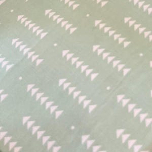 May include: A light green fabric with a repeating pattern of white triangles arranged in diagonal rows. Small white dots are scattered throughout the design. The fabric has a soft, textured appearance.