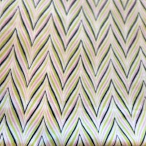 May include: A fabric with a repeating chevron pattern. The design features alternating stripes of black, light green, and pink on a cream-colored background. The pattern creates a zig-zag effect across the material.