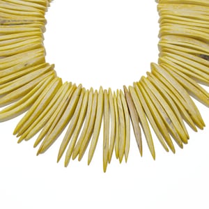 May include: A yellow necklace made of long, thin, pointed pieces of wood. The necklace is arranged in a fan shape.