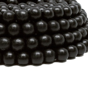 Puede incluir: Un collar de cuentas de madera negra. Las cuentas son redondas y lisas, y están dispuestas en espiral.