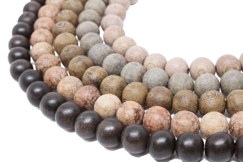 May include: A close-up of a wooden bead necklace with a gradient of colors, starting with dark brown and transitioning to light brown. The beads are round and smooth, and the necklace is made of multiple strands.