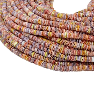 Könnte beinhalten: Eine Schnur aus bunten Muschelkernperlen in den Farben Rosa, Orange, Gelb und Lila. Die Perlen sind klein und flach und in einem kreisförmigen Muster angeordnet.