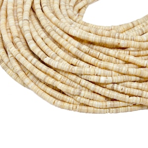 Puede incluir: Primer plano de un montón de cuentas beige en forma de disco. Las cuentas están ensartadas, formando una forma curva sobre un fondo blanco. Las cuentas tienen un aspecto natural y orgánico, lo que sugiere que están hechas de concha o hueso.