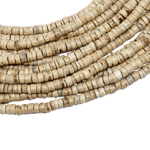 Puede incluir: Una hebra de cuentas de hueso beige natural, cada cuenta es redonda y ligeramente aplanada, creando una textura única. Las cuentas están enhebradas para formar un collar largo.