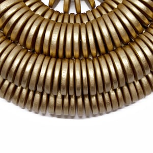 Puede incluir: Primer plano de un collar dorado con un diseño en capas. El collar está hecho de numerosas piezas metálicas pequeñas y redondeadas, dispuestas en arcos concéntricos. El fondo es blanco liso, resaltando la textura y la forma de la joya.