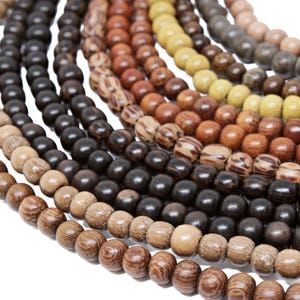 May include: A close-up of a multi-strand necklace made of wooden beads in various shades of brown, beige, and yellow. The beads are round and have a natural, rustic look.