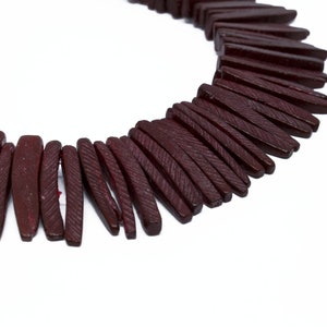 May include: A strand of dark red wooden beads, each bead is long and narrow with a textured surface.