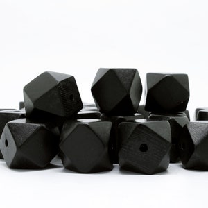 May include: A pile of black wooden beads with a geometric shape. Each bead has a hole in the center.