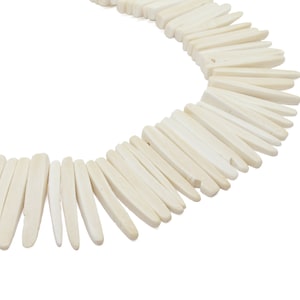 May include: Off-white necklace composed of numerous elongated, rectangular beads. The beads are arranged in a curved pattern, creating a circular shape. The necklace is set against a plain white background, highlighting the natural color and texture of the beads.