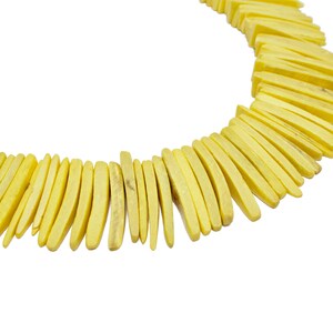 May include: A yellow necklace made of long, thin, wooden beads. The beads are arranged in a staggered pattern, creating a unique and eye-catching design.