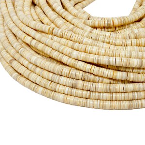 Puede incluir: Un hilo enrollado de cuentas planas y redondas en tonos crema y beige. Las cuentas son uniformes en tamaño y forma, con una textura ligeramente irregular. Las cuentas probablemente se utilizan para la fabricación de joyas u otras manualidades.