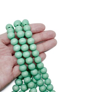 Puede incluir: Una hebra de cuentas de madera de color verde claro, sostenida en una mano. Las cuentas son redondas y lisas.