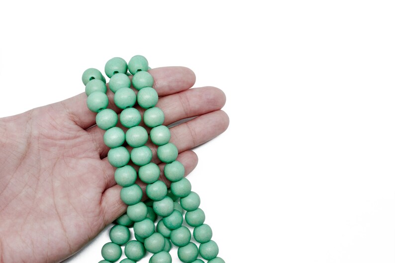 Puede incluir: Una hebra de cuentas de madera de color verde claro, sostenida en una mano. Las cuentas son redondas y lisas.