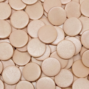 May include: A close-up of a pile of round, light brown wooden counters. The counters are smooth and have a slightly textured surface.
