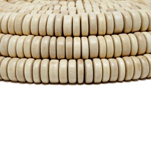 Puede incluir: Primer plano de una hebra de cuentas de madera natural. Las cuentas son redondas y tienen un acabado liso y pulido. Están dispuestas en un patrón circular, creando una textura visualmente atractiva.