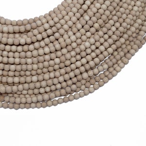 Może przedstawiać: Sznur naturalnych drewnianych koralików w jasnobrązowym kolorze. Korale są okrągłe i gładkie, a nawleczone są na przezroczystą nić.