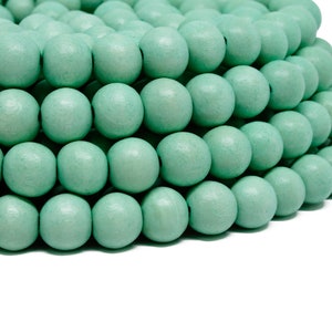 Puede incluir: Primer plano de un mont&oacute;n de cuentas de madera de color verde claro. Las cuentas son redondas y lisas, y est&aacute;n dispuestas en un patr&oacute;n circular.