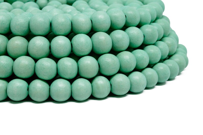 Puede incluir: Primer plano de un mont&oacute;n de cuentas de madera de color verde claro. Las cuentas son redondas y lisas, y est&aacute;n dispuestas en un patr&oacute;n circular.