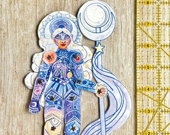 Könnte beinhalten: Eine Papierpuppe einer himmlischen Kriegerin mit einem Halbmondstab. Die Puppe trägt eine blaue und violette Rüstung mit Sternen und Planeten. Die Puppe hält einen Stab mit einem Halbmond oben. Die Puppe ist von einer blauen und violetten Wolke umgeben.