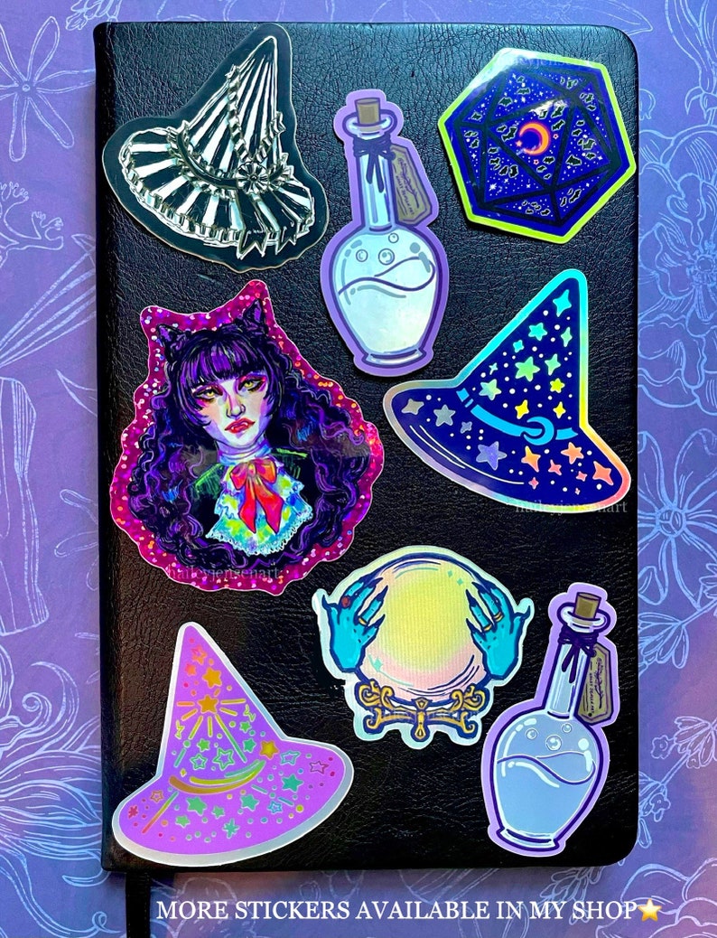 K&ouml;nnte beinhalten: Eine Sammlung holografischer Aufkleber mit einem Hexenhut, einer Zaubertrankflasche, einer Kristallkugel und einer Figur mit lila Haaren. Die Aufkleber befinden sich auf einem schwarzen Notizbuch mit violettem Hintergrund.