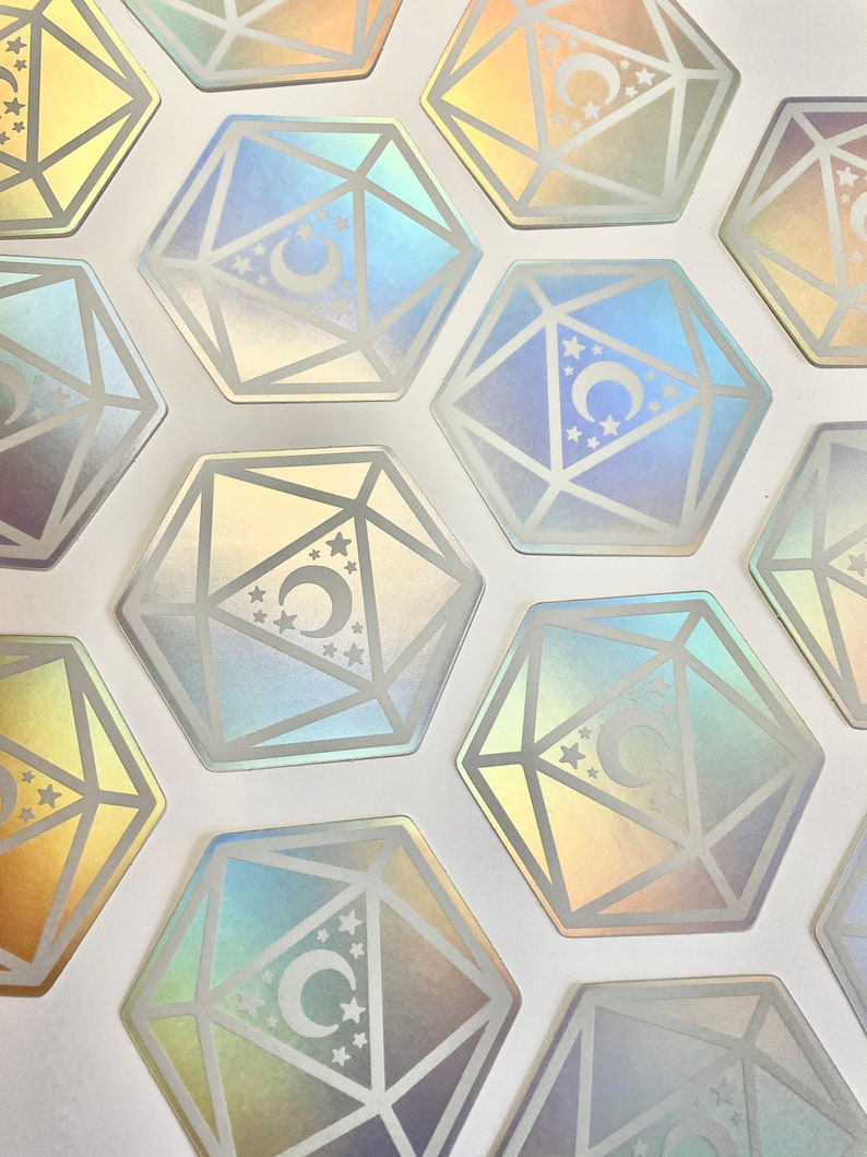 May include: A set of iridescent holographic stickers featuring a crescent moon and stars inside a geometric design resembling a twenty-sided die.
