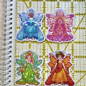 May include: Four colorful fairy stickers. The stickers feature illustrations of fairies in various outfits and colors, including blue, pink, green, and orange. Each fairy has detailed wings and unique attire.