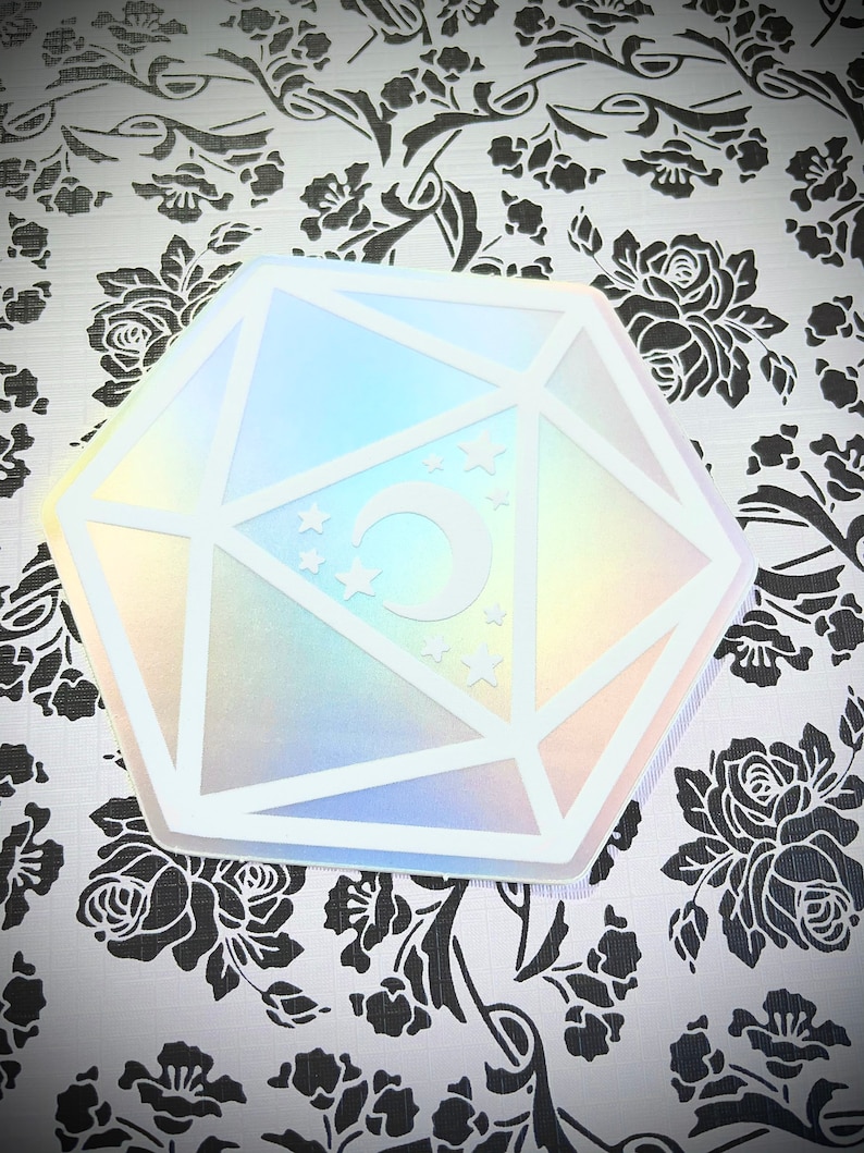 May include: A white iridescent sticker with a holographic finish, shaped like a twenty-sided die with a crescent moon and stars inside.