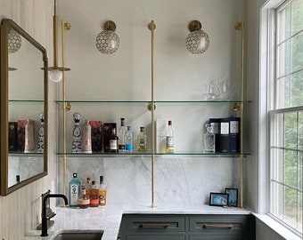 May include: A home bar with a white marble countertop, green cabinets, and glass shelves with gold accents. The shelves are stocked with bottles of liquor and glassware. A small rug is on the floor.