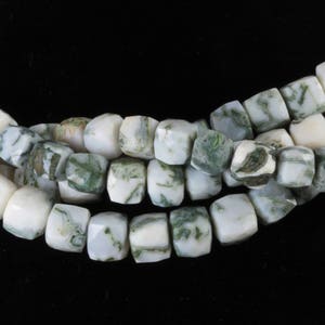 Puede incluir: Primer plano de un collar o pulsera de cuentas de piedras preciosas blancas y verdes. Las cuentas son cuadradas con bordes redondeados, y los patrones verdes varían. Las cuentas están ensartadas.