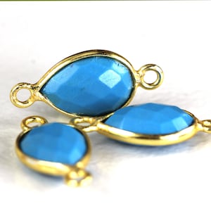 May include: Three gold-plated teardrop-shaped jewelry components with faceted turquoise-colored stones. Each component has a loop at the top and bottom for attaching to other jewelry pieces. The components are displayed on a white background.