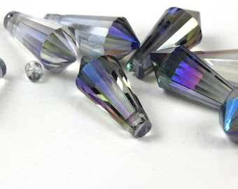 May include: A collection of iridescent crystal beads in a variety of shapes. The beads are faceted, reflecting light with a rainbow effect. The shapes include elongated, cone-like forms and a small, round bead. The beads are scattered on a white surface.