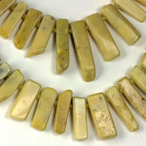 May include: A necklace featuring two strands of rectangular, light yellow-green beads. The beads are strung together with a light-colored string. The necklace has a natural, earthy aesthetic, suitable for casual or bohemian styles.