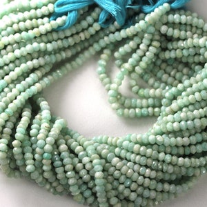 May include: Strands of small, faceted, pale green beads. The beads are strung together, forming a bundle with a turquoise tassel at the top. The beads have a slightly irregular shape and a matte finish.
