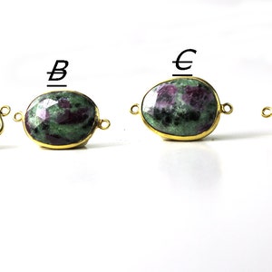 May include: Four gemstone pendants with gold-colored settings. The gemstones are a mix of green and red. Each pendant has a different shape: a triangle, an oval, a freeform shape, and a rounded oval. Each has loops for attaching to a chain.
