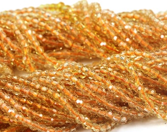 May include: Close-up of strands of faceted, amber-colored beads. The beads are strung together, creating a textured, layered effect. The beads have a sparkling, iridescent quality, reflecting light. The overall effect is warm and inviting, suggesting jewelry or craft supplies.