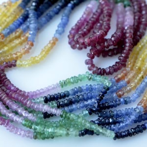 May include: Strands of colorful gemstone beads in shades of yellow, blue, green, purple, and red. The beads are small and faceted, strung together to create a necklace or bracelet. The background is white.
