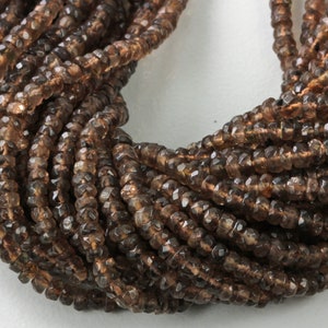 May include: Close-up of a bundle of faceted, brown gemstone beads. The beads are strung together, creating a textured, layered effect. The color ranges from light to dark brown, with a slight shimmer.