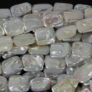 May include: Close-up of a collection of iridescent, square-shaped beads. The beads have a pearlescent sheen, reflecting light with a range of colors. The beads are arranged closely together, creating a textured surface.