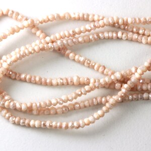 May include: Strands of faceted, peach-colored beads. The beads are small and uniform in size, strung together to create multiple strands. The beads have a subtle sparkle and are arranged against a white background.