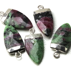 May include: Five faceted ruby pendants with silver-colored metal caps and loops. The pendants have a mix of red, green, and black colors. The pendants are on a white background.