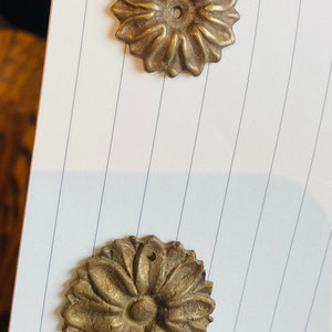 Peut inclure: Deux décorations florales en métal doré. La décoration du haut a une forme plus pointue, en forme d'étoile. La décoration du bas a une forme plus arrondie, en forme de fleur.