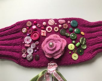 Lila Nestelmuff mit rosa gehäkelter Rose vielen Perlen Knöpfen, Bändchen und viele Elemente innen wie außen
