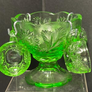 May include: A vintage green glass punch bowl with four matching cups. The bowl and cups have a delicate etched floral design. The cups hang from the bowl with metal hooks.