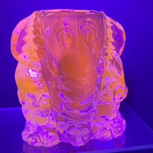 May include: A clear glass sculpture of a dog with a textured surface. The sculpture is illuminated with a purple light, making it appear pink and orange.